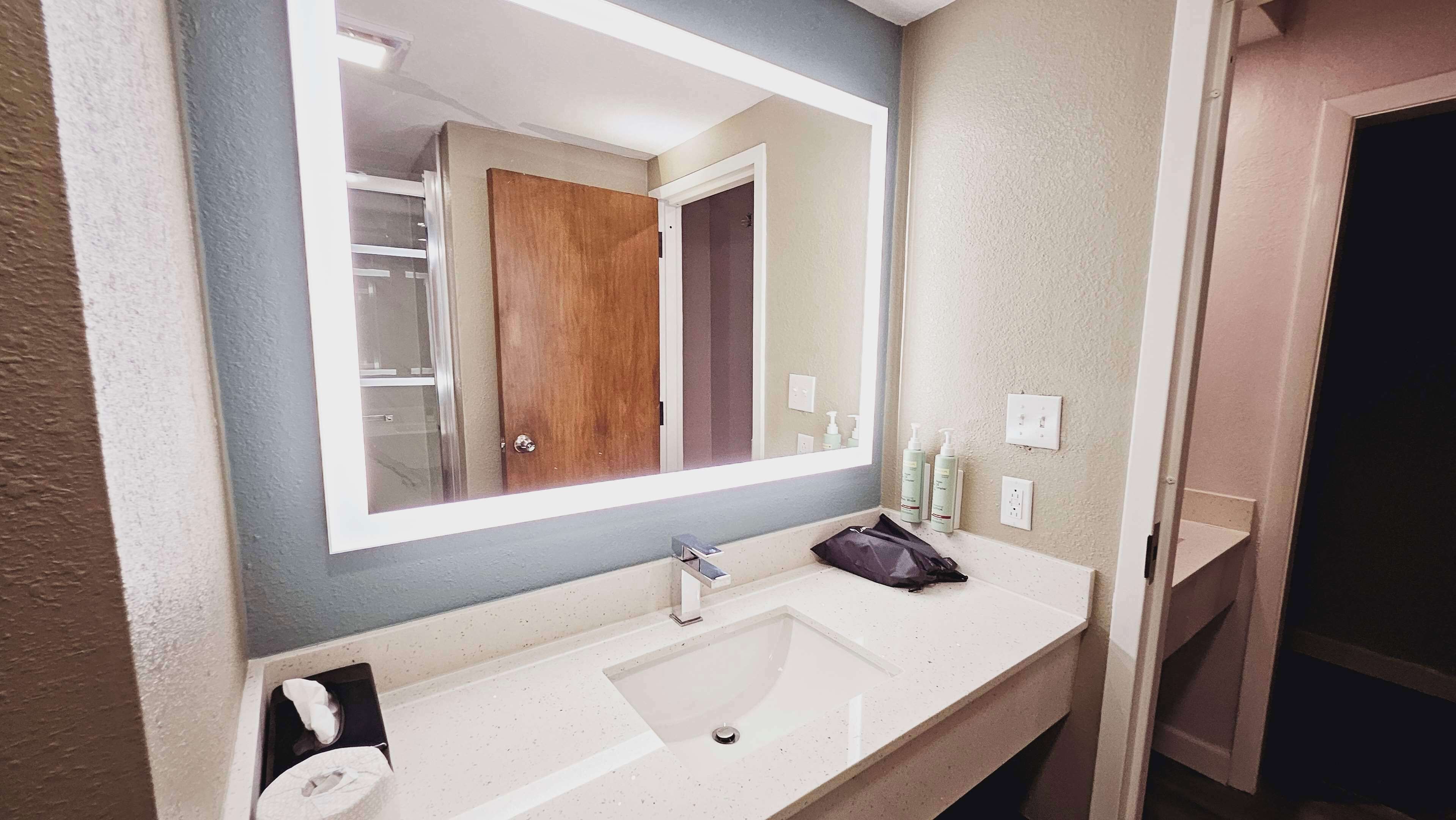 A bathroom with a large mirror, a sink, and toiletries on the counter.