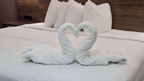 Ein ordentlich gemachtes Bett mit weißen Leinentüchern und zwei Handtüchern, die zu Schwänen geformt sind.