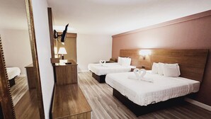 Habitación de hotel con dos camas, cabecero de madera, espejo, escritorio con lámpara y televisor montado en la pared.