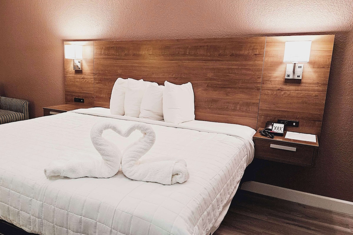 A hotel room with a large bed, two bedside tables, a chair, and a wooden headboard.