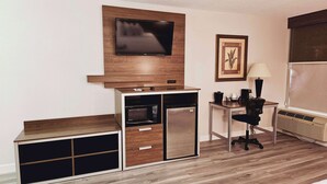 Una kitchenette compacta con microondas, refrigerador y una mesita con lámpara.