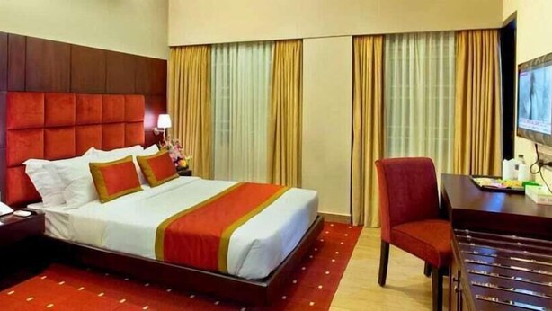 A hotel room with a large bed, a desk, a chair, and a television.