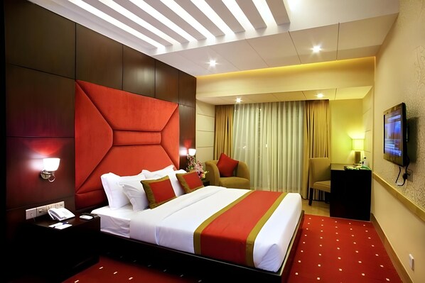 Una habitación de hotel con una cama grande, un escritorio, una silla, un televisor y una ventana con cortinas.