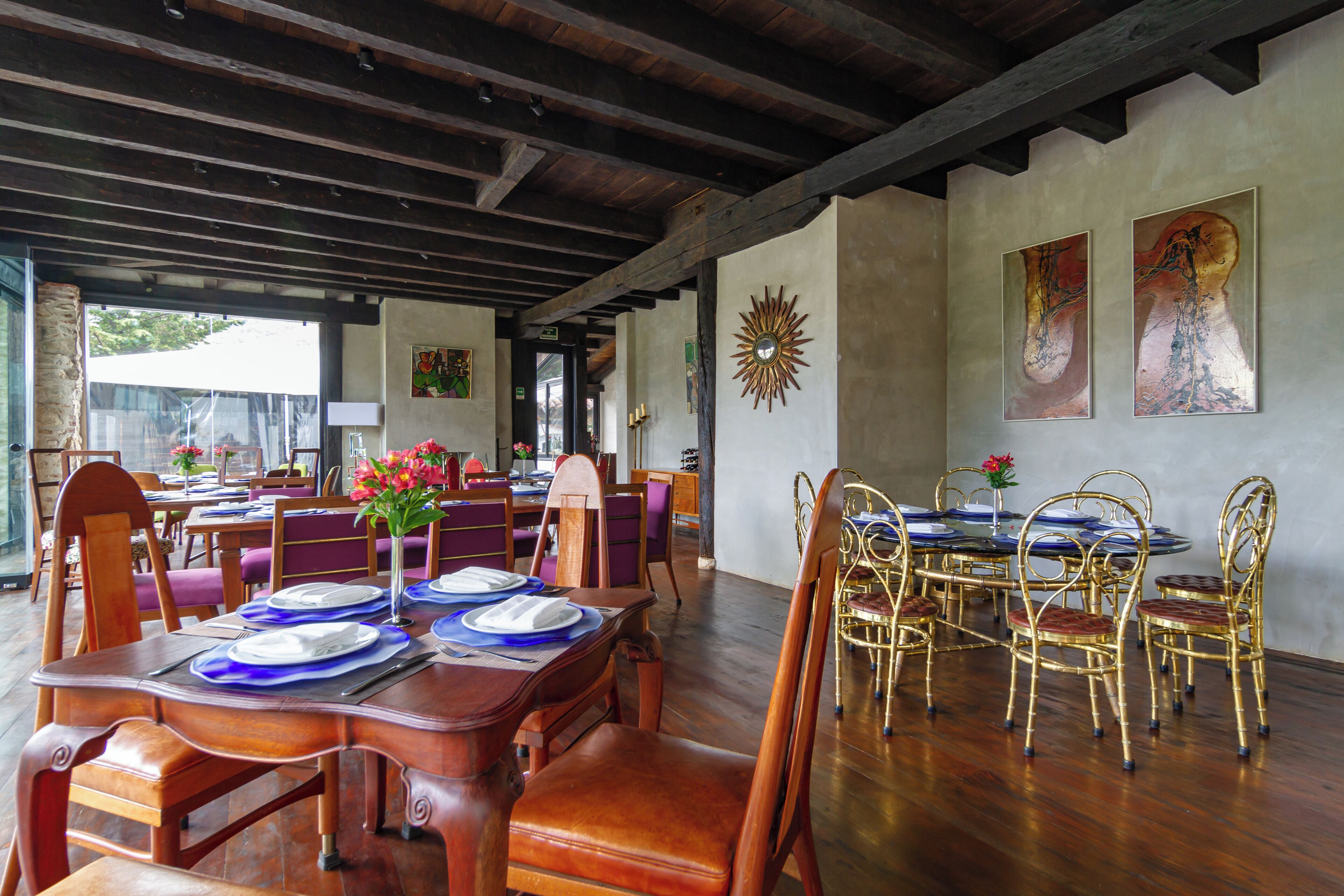 A dining area with wooden tables and chairs, a sunburst wall decoration, and artwork on the walls.