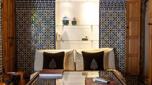 A room with a sofa, a glass coffee table, and patterned tile walls. - Dar El Bali (Fes)