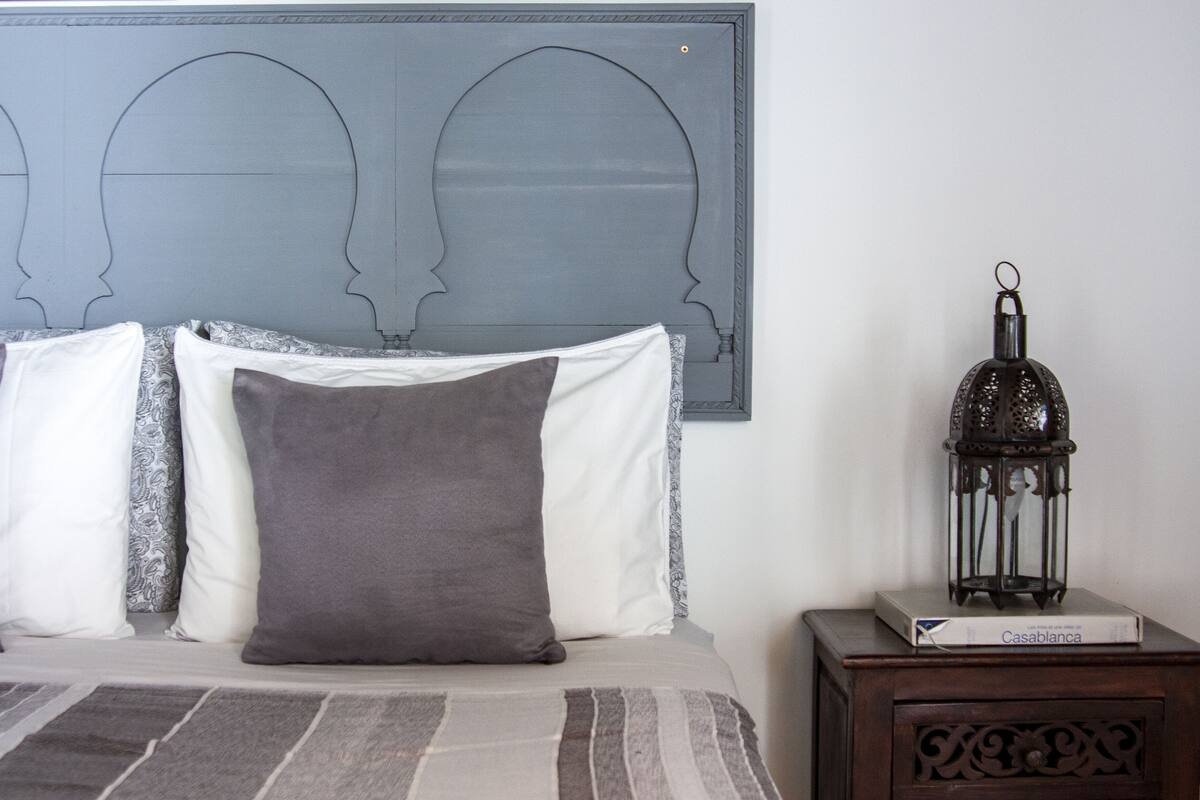 A bed with patterned bedding, a decorative wall piece, and a nightstand with a lantern and a box.