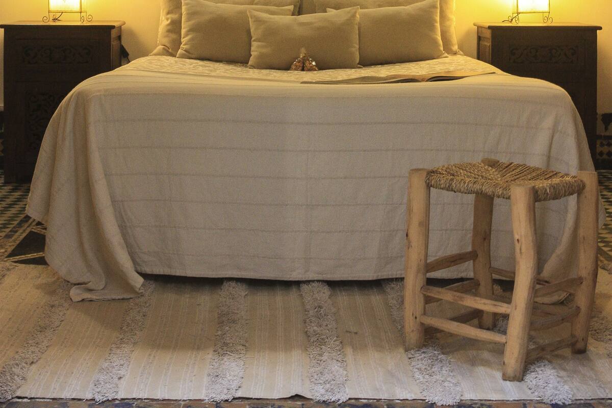 A bedroom with a bed, two bedside tables, a chair, a wall-mounted picture, and two wall-mounted lamps.