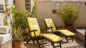 A sunlit patio with two yellow cushioned chairs, potted plants, and a tiled floor. - Dar El Bali (Fes)