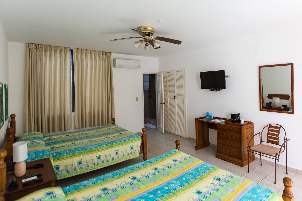 Une chambre d’hôtel avec deux lits, un bureau, une chaise, une télévision et un ventilateur de plafond.