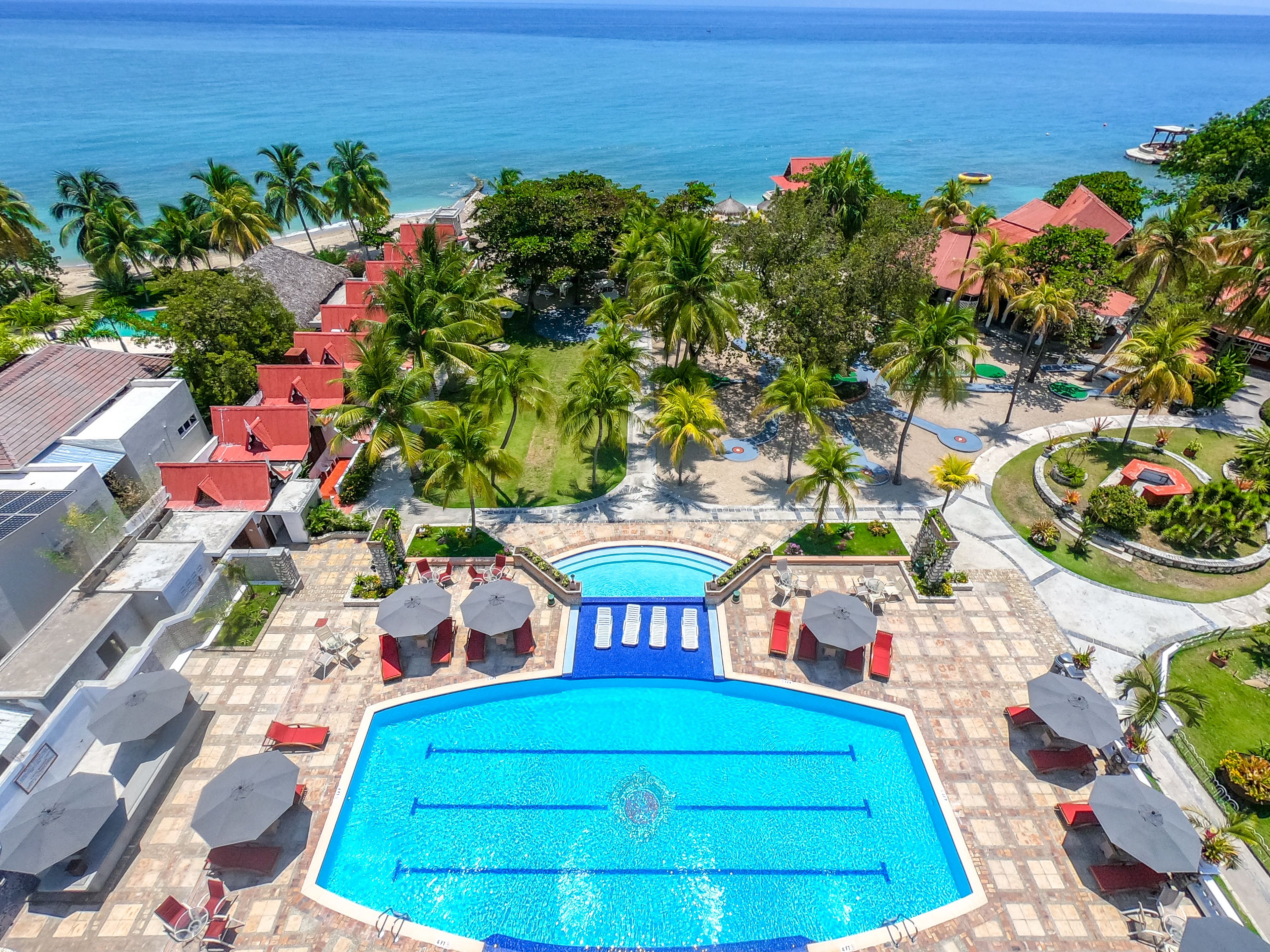 Vue aérienne d’un complexe hôtelier doté d’une piscine centrale, de palmiers et d’une plage.