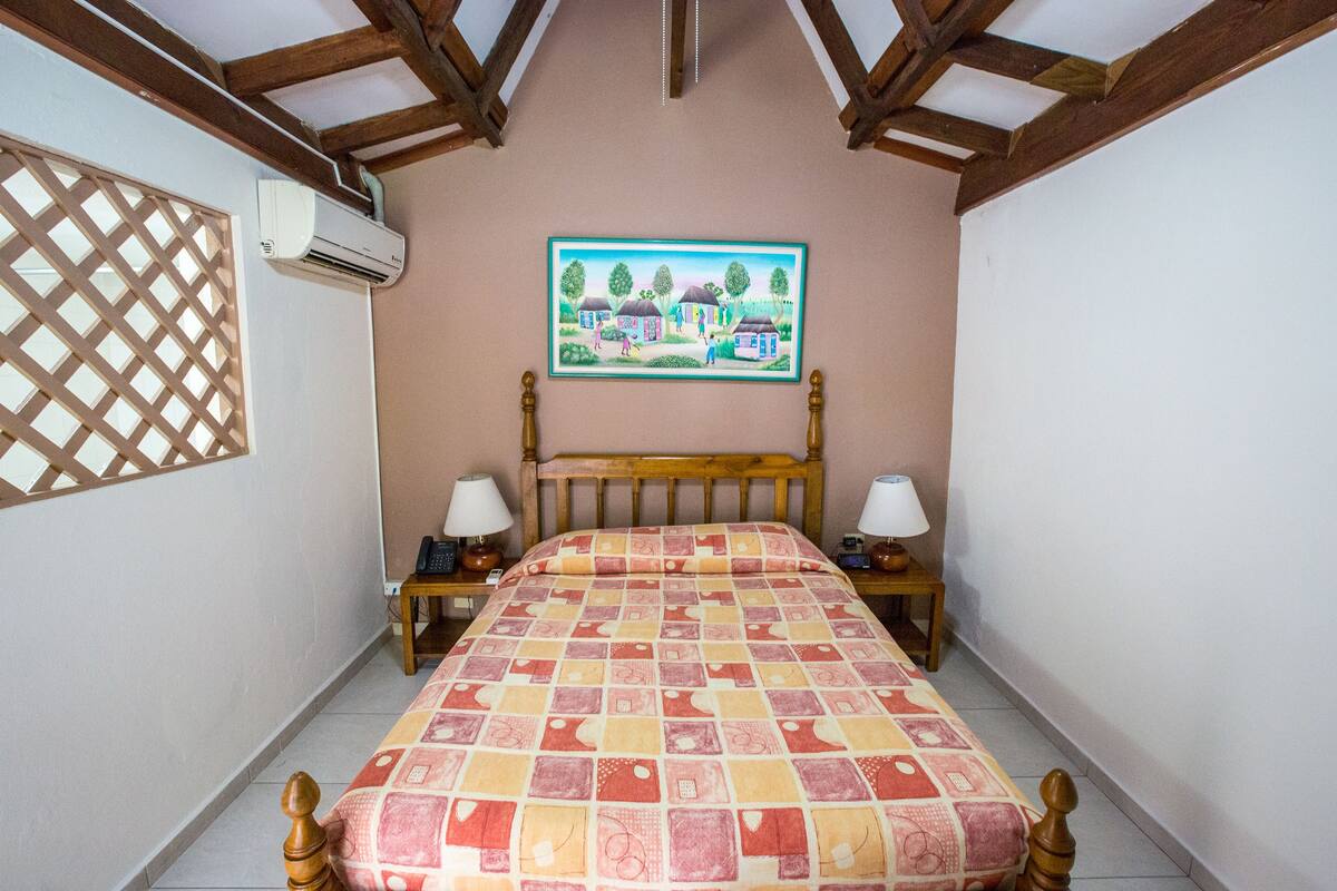 Une chambre à coucher avec un lit en bois, deux tables de chevet avec des lampes, un appareil de climatisation et un tableau accroché au mur.