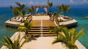 A wooden pier leading to a beach with lounge chairs and palm trees. - Moulin Sur Mer (Saint-Marc)