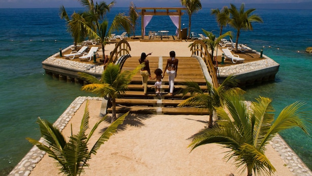 A wooden pier leading to a beach with lounge chairs and palm trees. - Moulin Sur Mer (Saint-Marc)