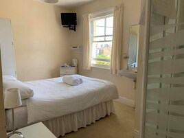 Una habitación de hotel con cama, mesita de noche con lámpara, ventana con cortinas, lavamanos y espejo.