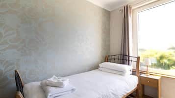 Una cama individual con sábanas blancas, un cabecero de madera y una mesita de noche con lámpara.