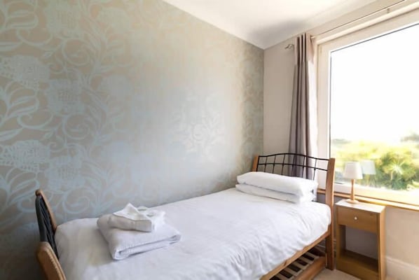 A single bed with white linens, a wooden headboard, and a nightstand with a lamp.