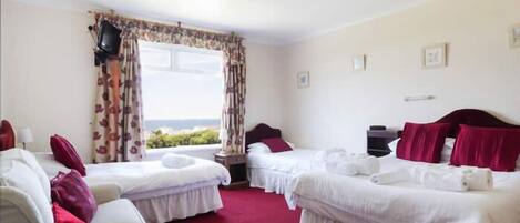 A hotel room with two single beds, a sofa, a desk, and a view of the sea.