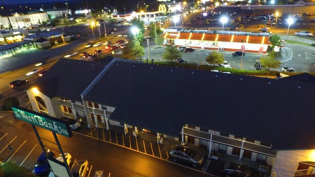 A hotel with a large parking lot, a McDonald's restaurant across the street, and a street sign for 'The West Bank Inn'. - West Bank Inn (Augusta)