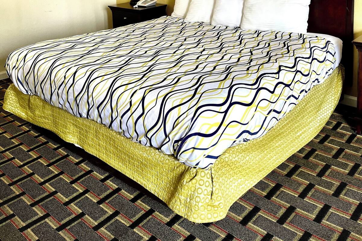 A hotel room with a large bed, a nightstand, a lamp, and two framed pictures on the wall.