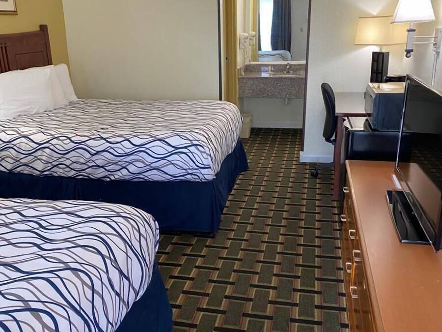 Ein Hotelzimmer mit zwei Betten, einem Schreibtisch, einem Stuhl, einem Fernseher und einem Badezimmer.