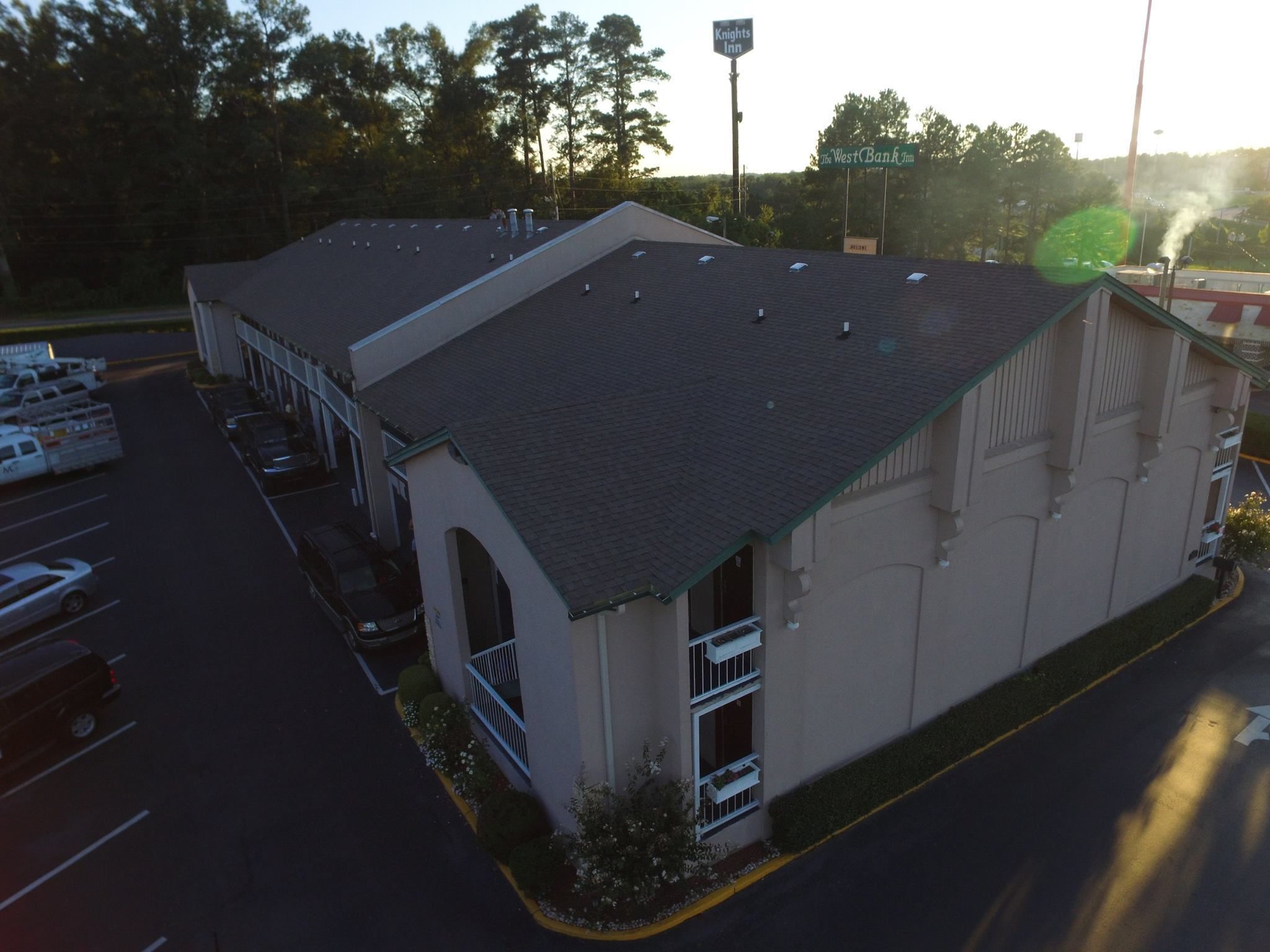 A building with a flat roof, a large arched entrance, and a parking lot with several vehicles.