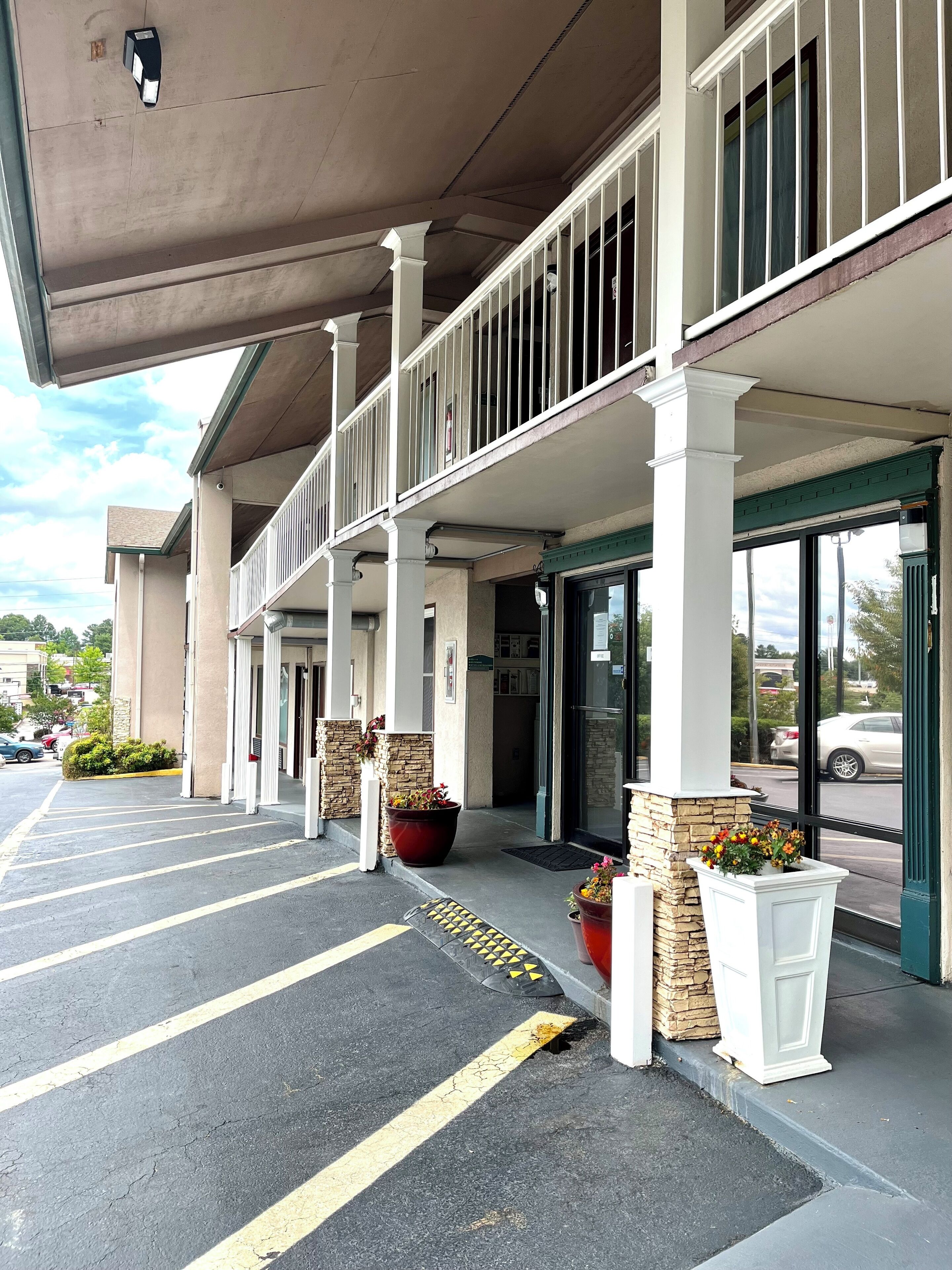 A hotel entrance with a covered parking area, a balcony with railings, and potted plants.