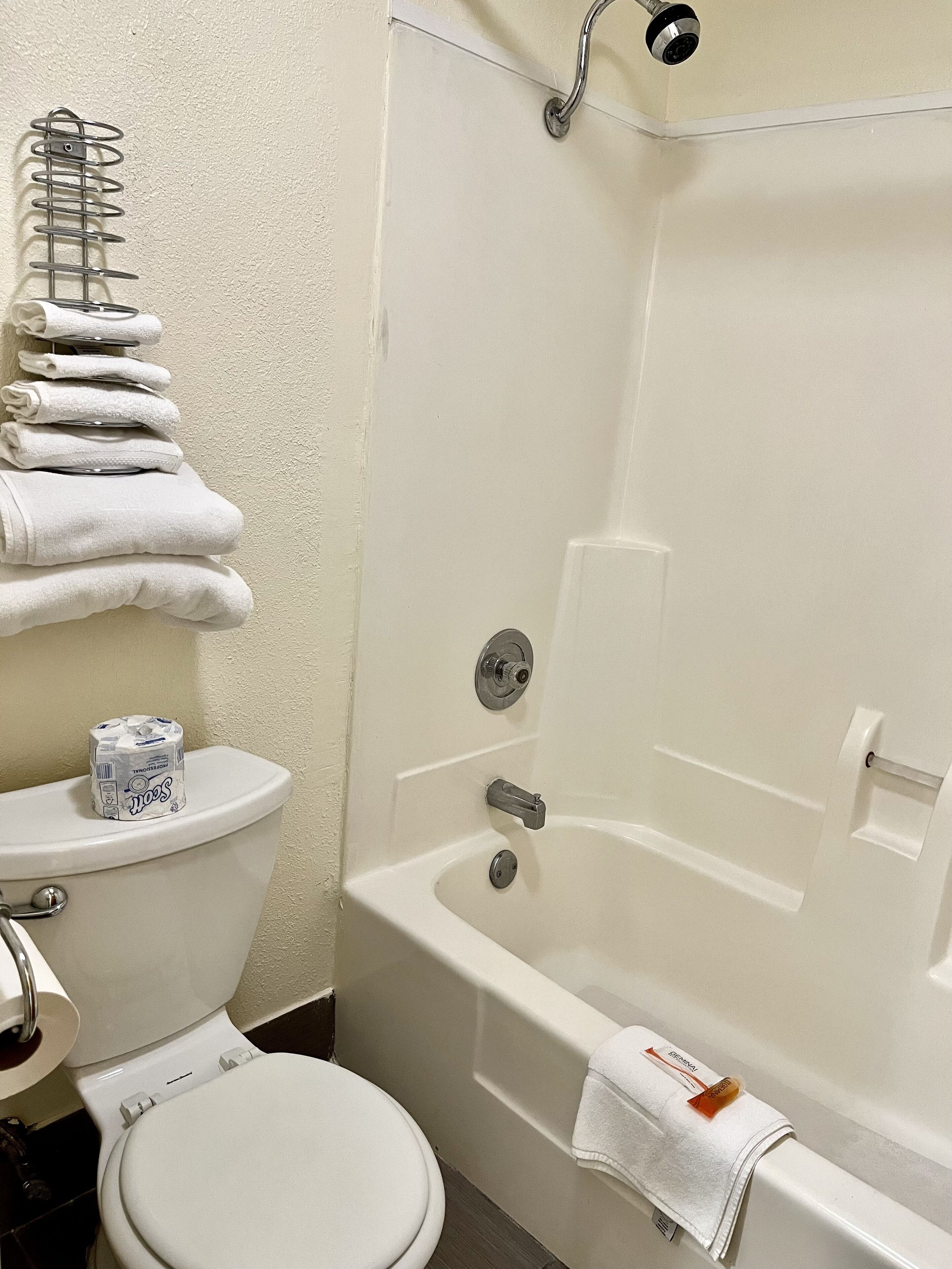 A bathroom with a toilet, a stack of white towels, and a bathtub.