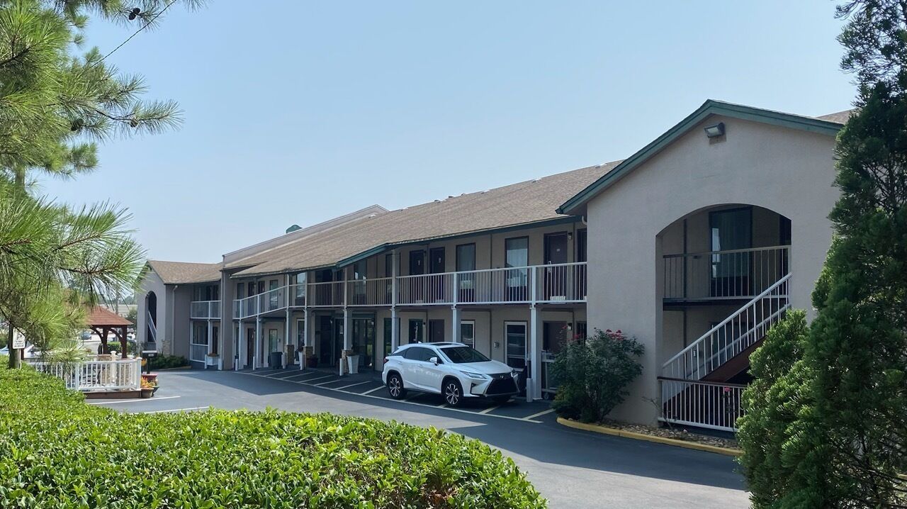 A motel with multiple balconies, a covered parking area, and a white car parked in front.