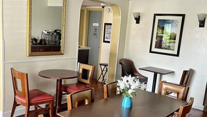 A dining area with a large wooden table, red cushioned chairs, a vase with flowers, and a framed picture on the wall. - West Bank Inn (Augusta)