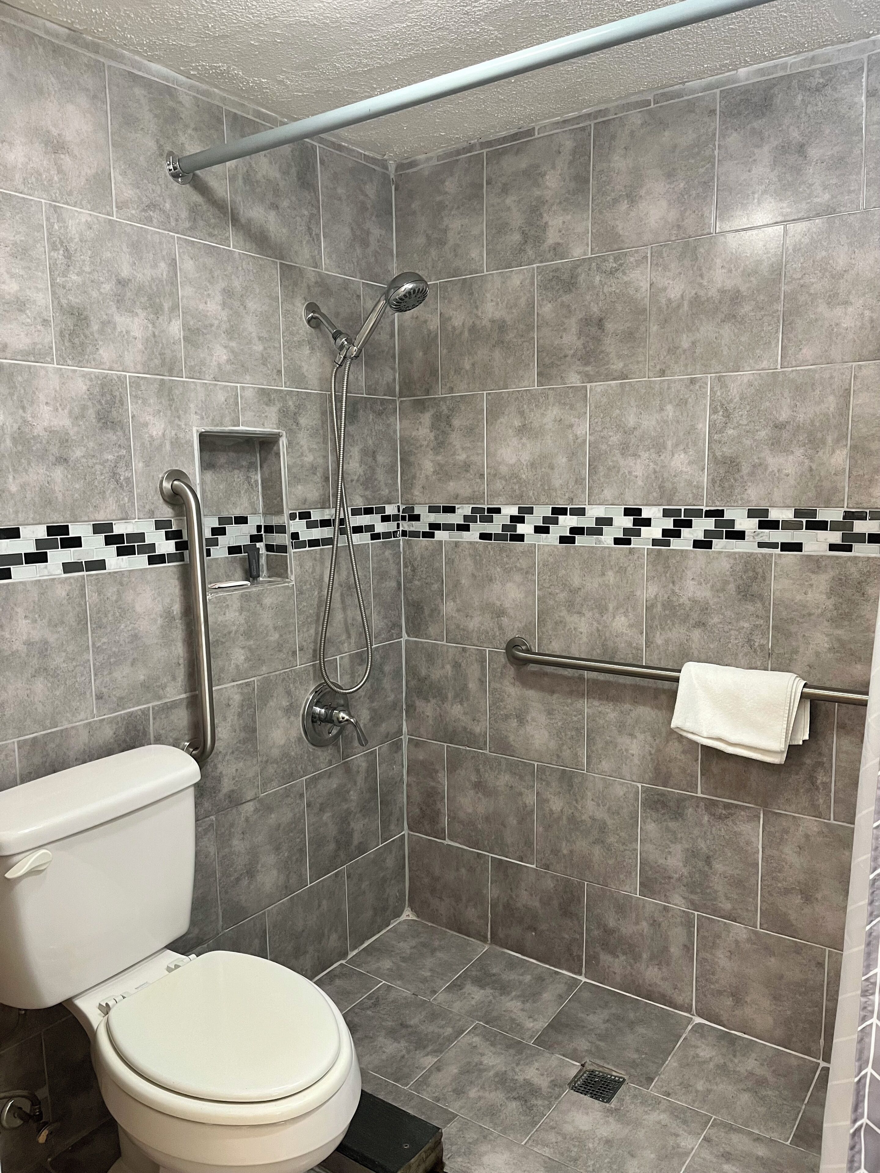 A bathroom with a shower, toilet, and a towel rack.
