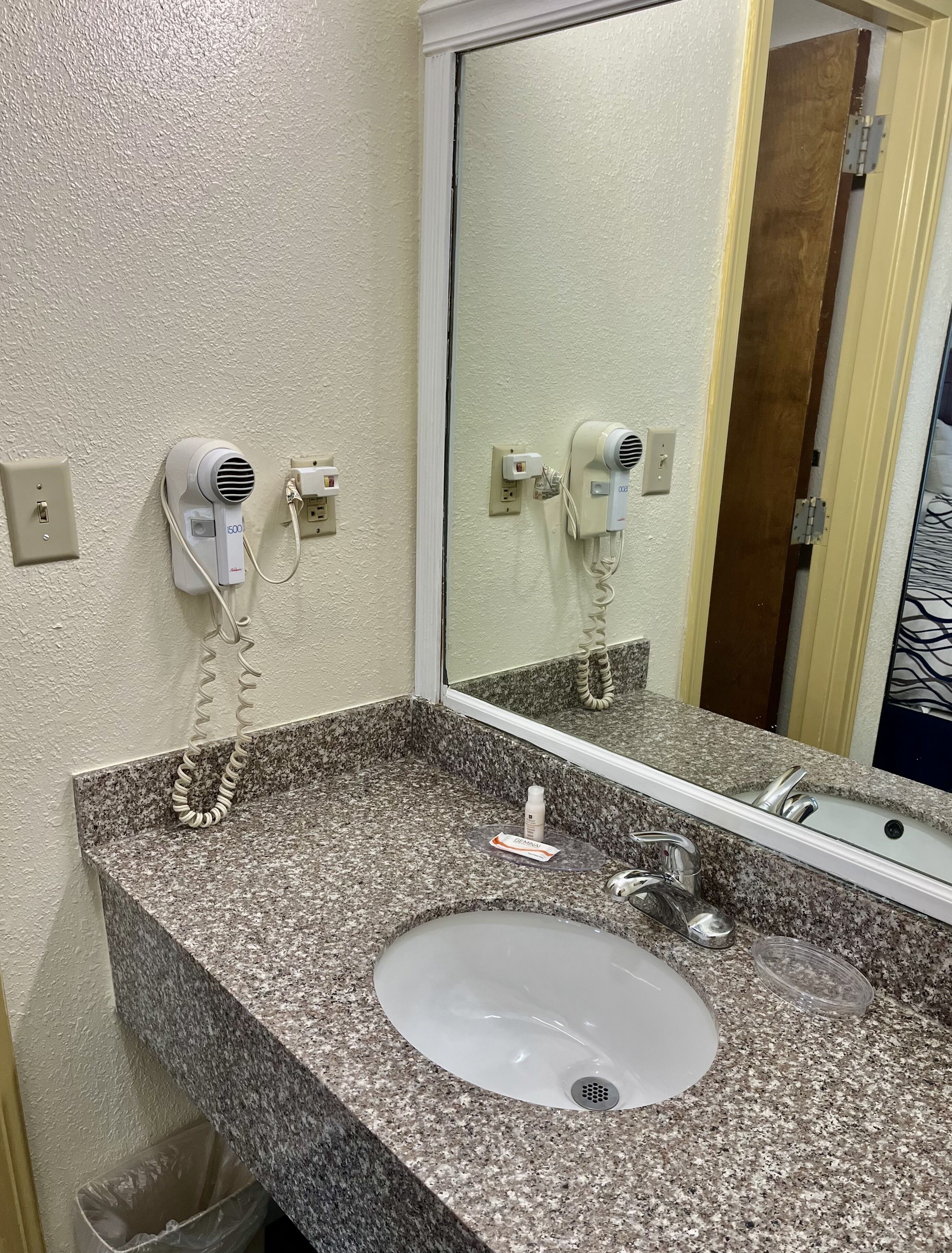A bathroom with a granite countertop, a sink, a mirror, and two hair dryers mounted on the wall.