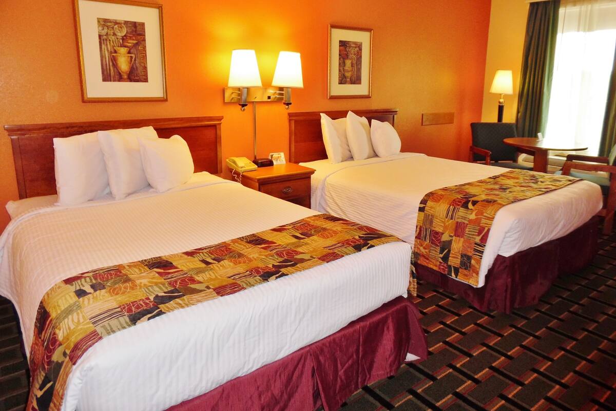 A hotel room with two beds, a nightstand, a telephone, and two wall-mounted lamps.