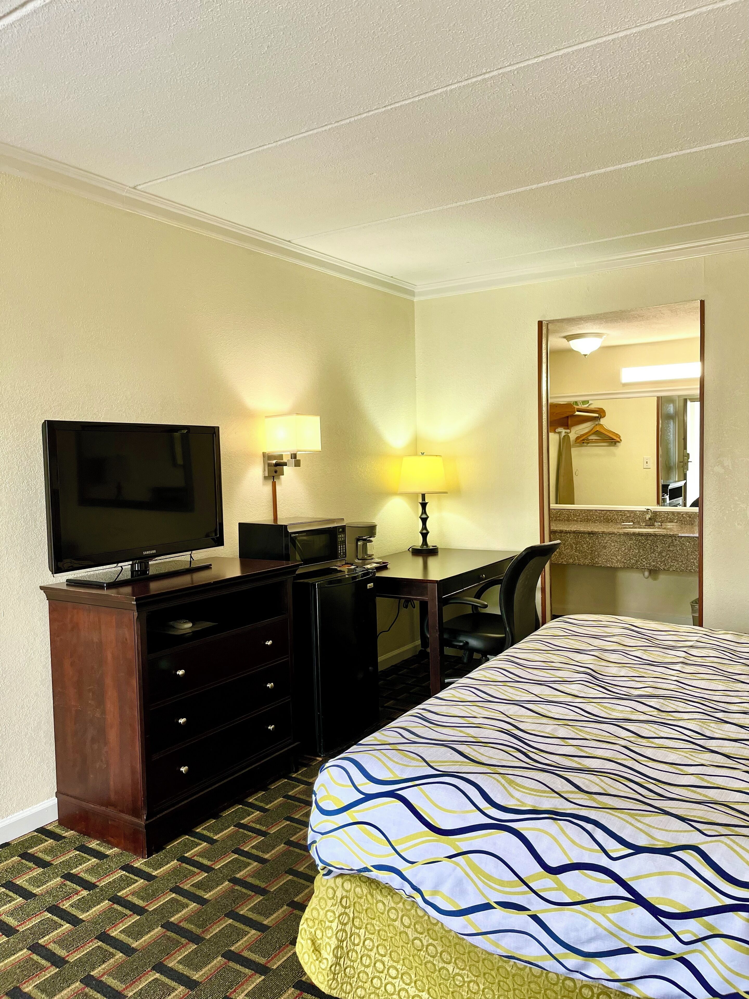 A hotel room with a bed, a desk with a television, a lamp, and a mirror.