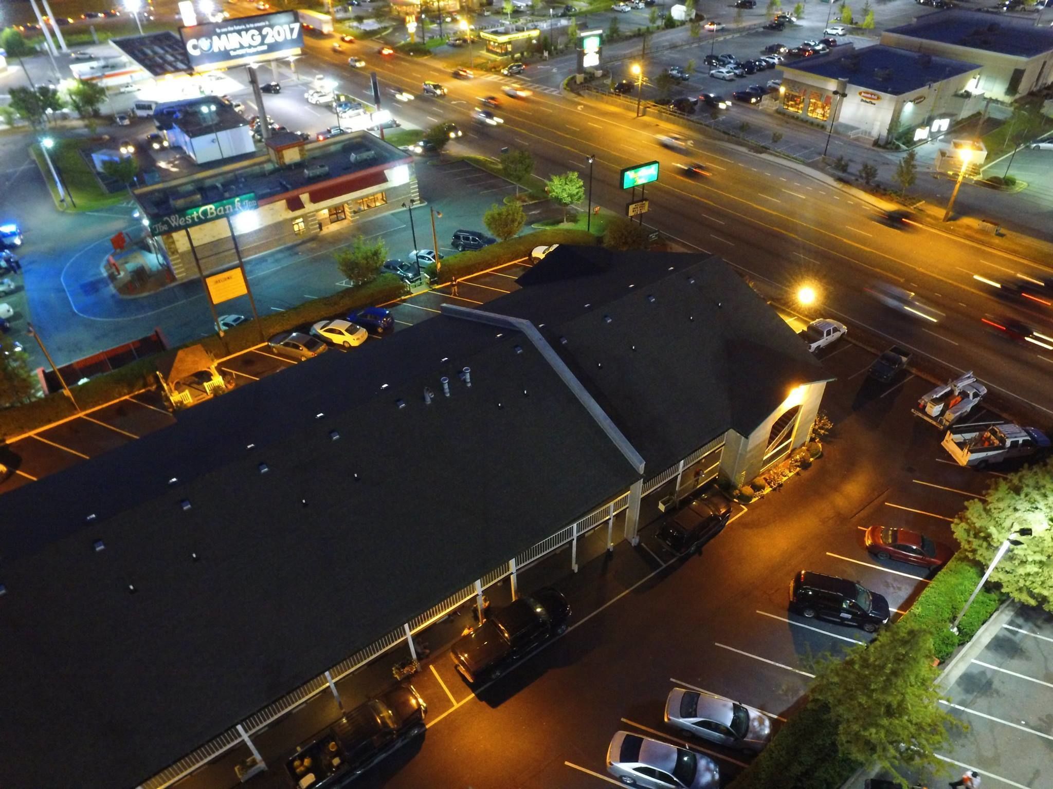 An aerial view of a parking lot with multiple cars, a large building with a flat roof, and a sign indicating a bank.