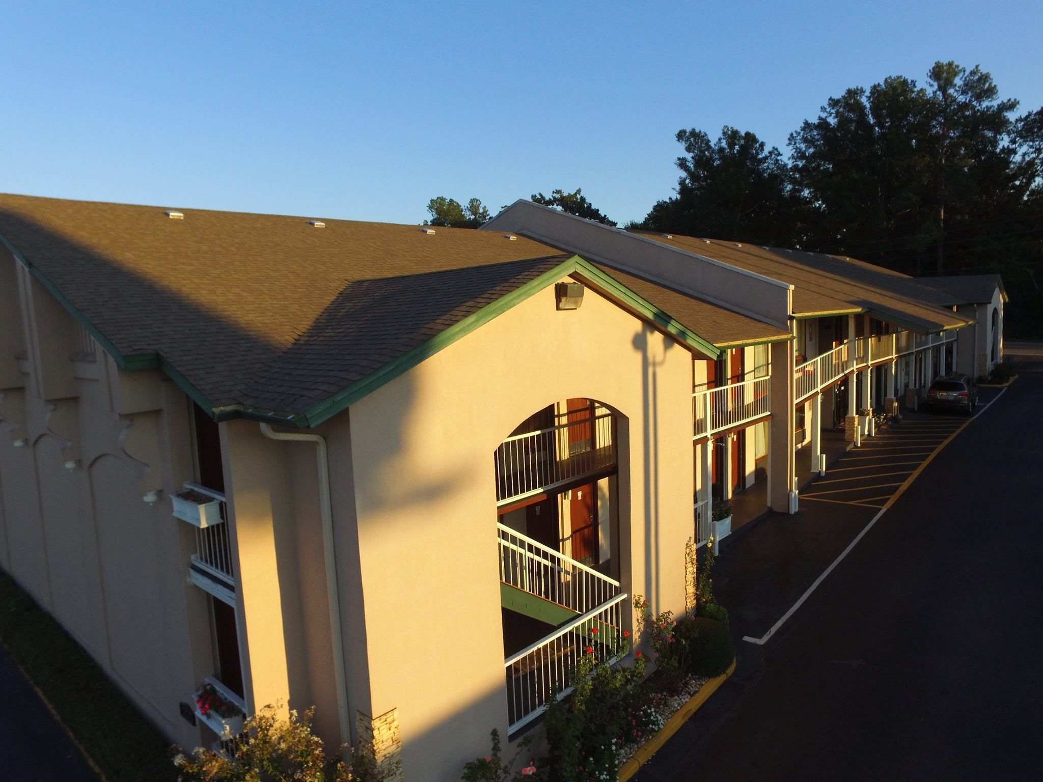 A row of motel buildings with a central walkway, large windows, and a parking lot.