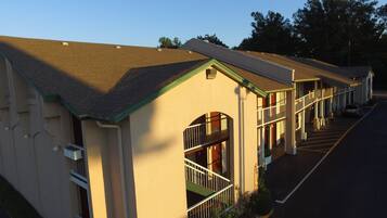 A row of motel buildings with a central walkway, large windows, and a parking lot.
