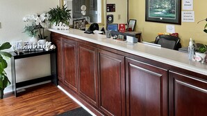 A reception area with a wooden reception desk, a clock, and a 'No Pets Allowed' sign. - West Bank Inn (Augusta)