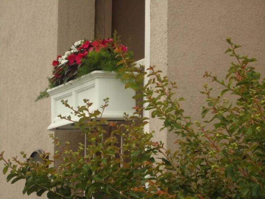 Ein weißer Blumenkasten an einer Außenwand eines Gebäudes.