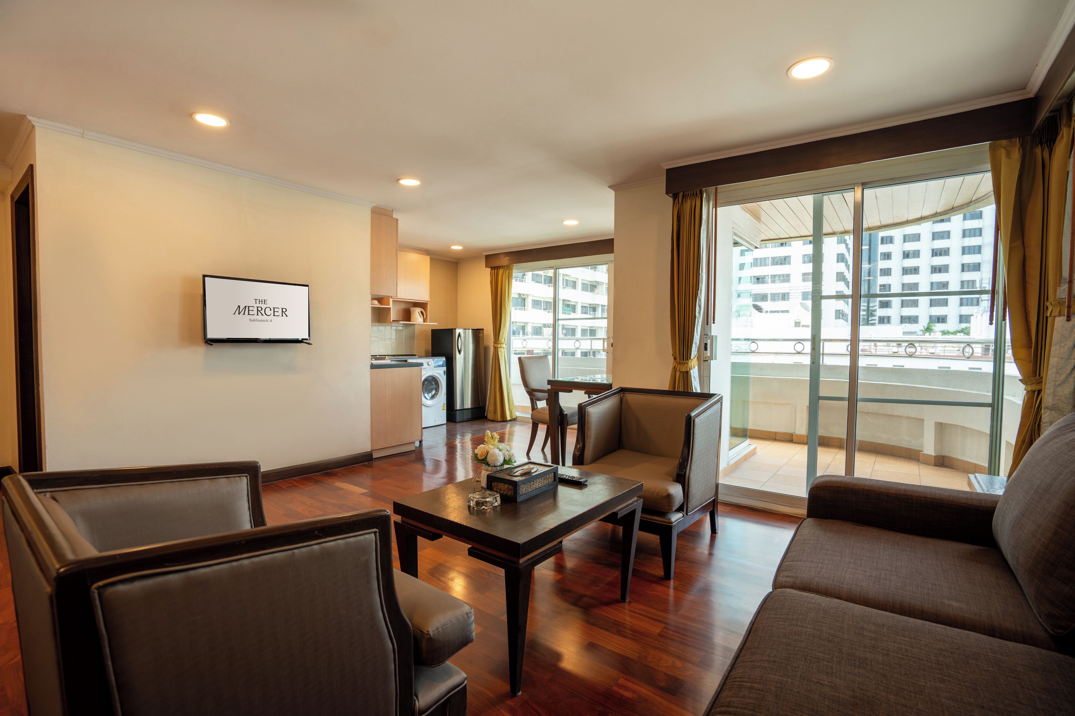 Habitación de hotel con sala de estar, mesa de comedor, sofá, televisor montado en la pared y balcón con vista a la ciudad.