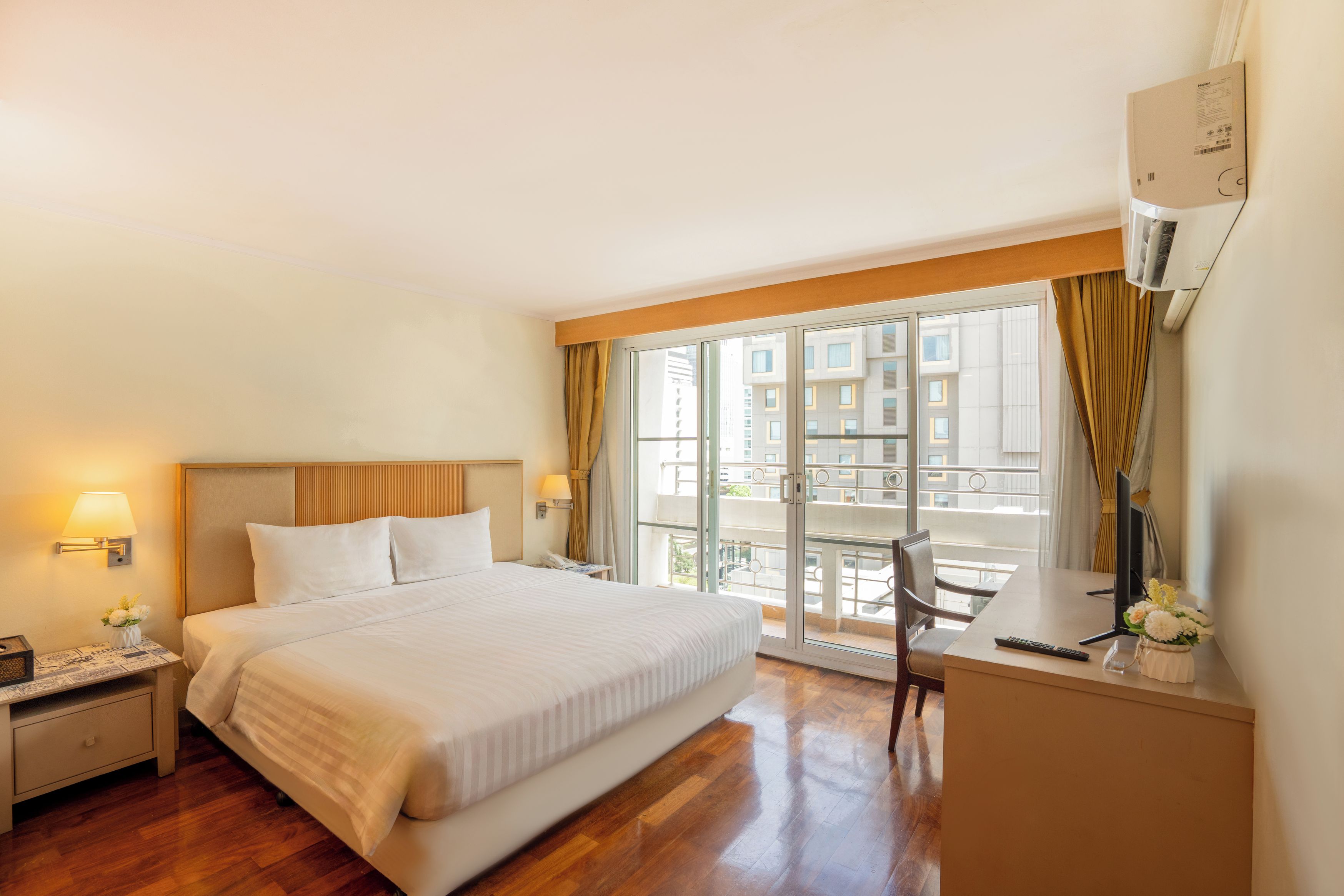 A hotel room with a bed, bedside table, lamp, and a view of the city through large windows.