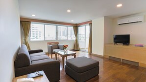 Una habitación de hotel moderna con sofá, reposapiés y una pequeña mesa con un florero.