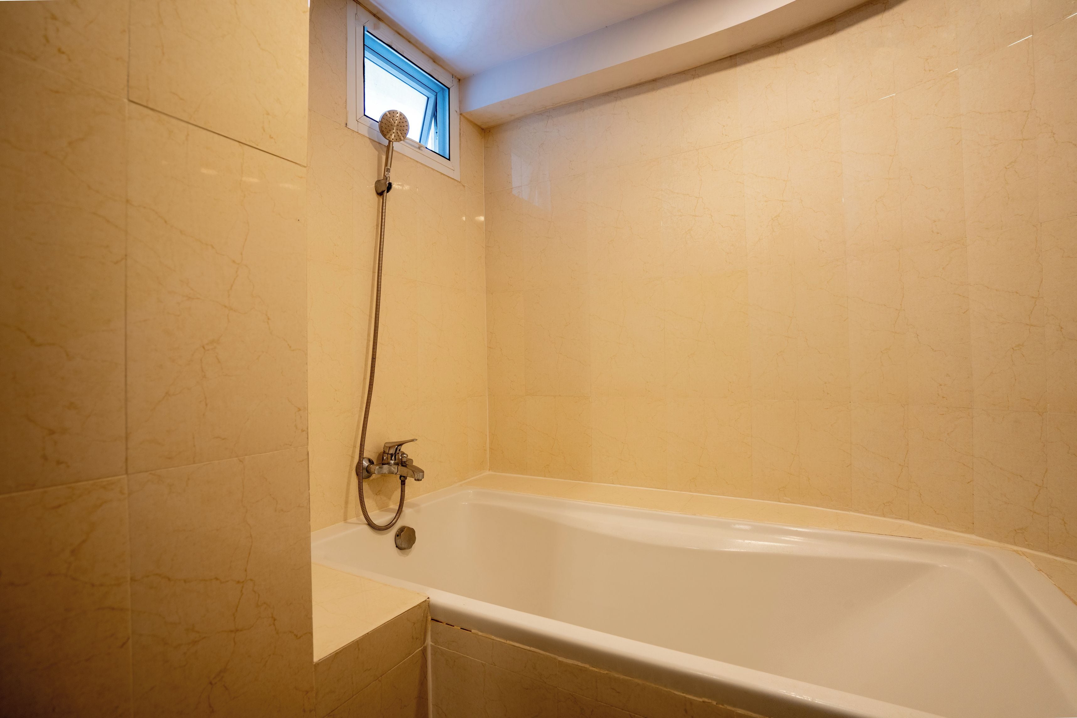 A bathroom with a bathtub, a showerhead, and a window.