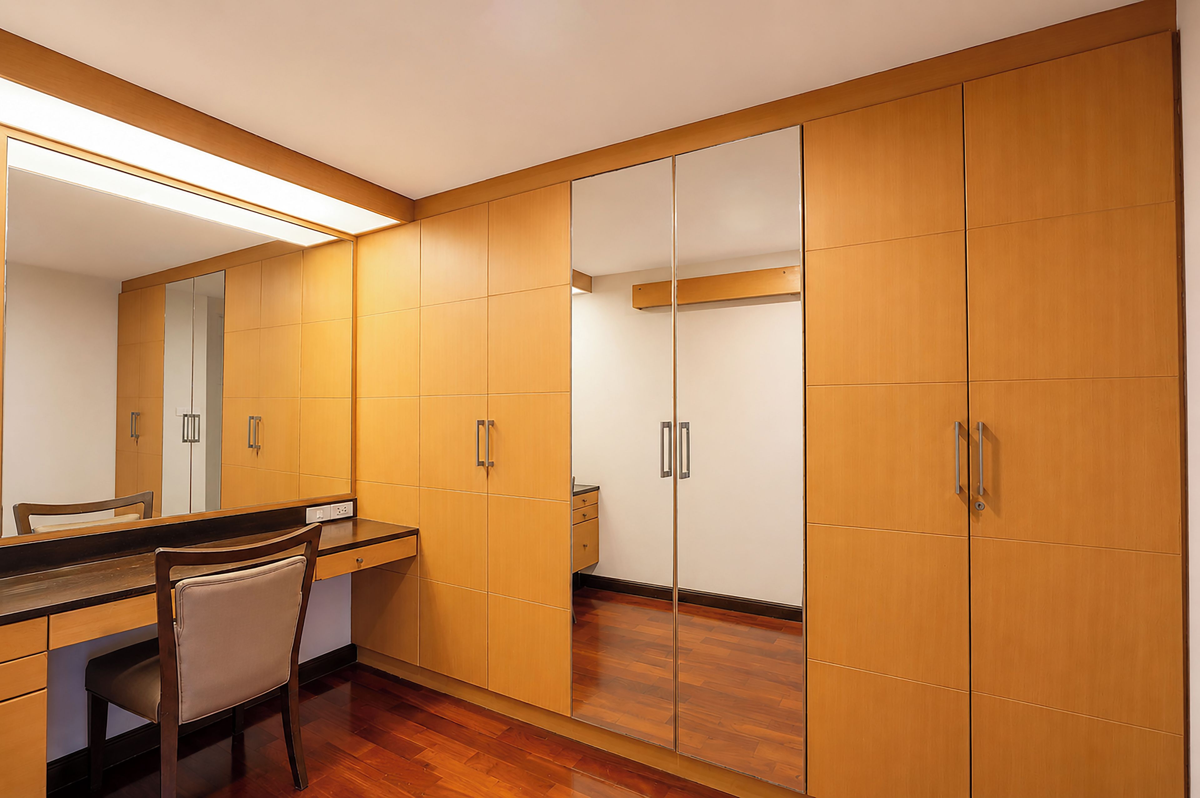 A room with a wooden wardrobe, a mirror, a desk, and a chair.