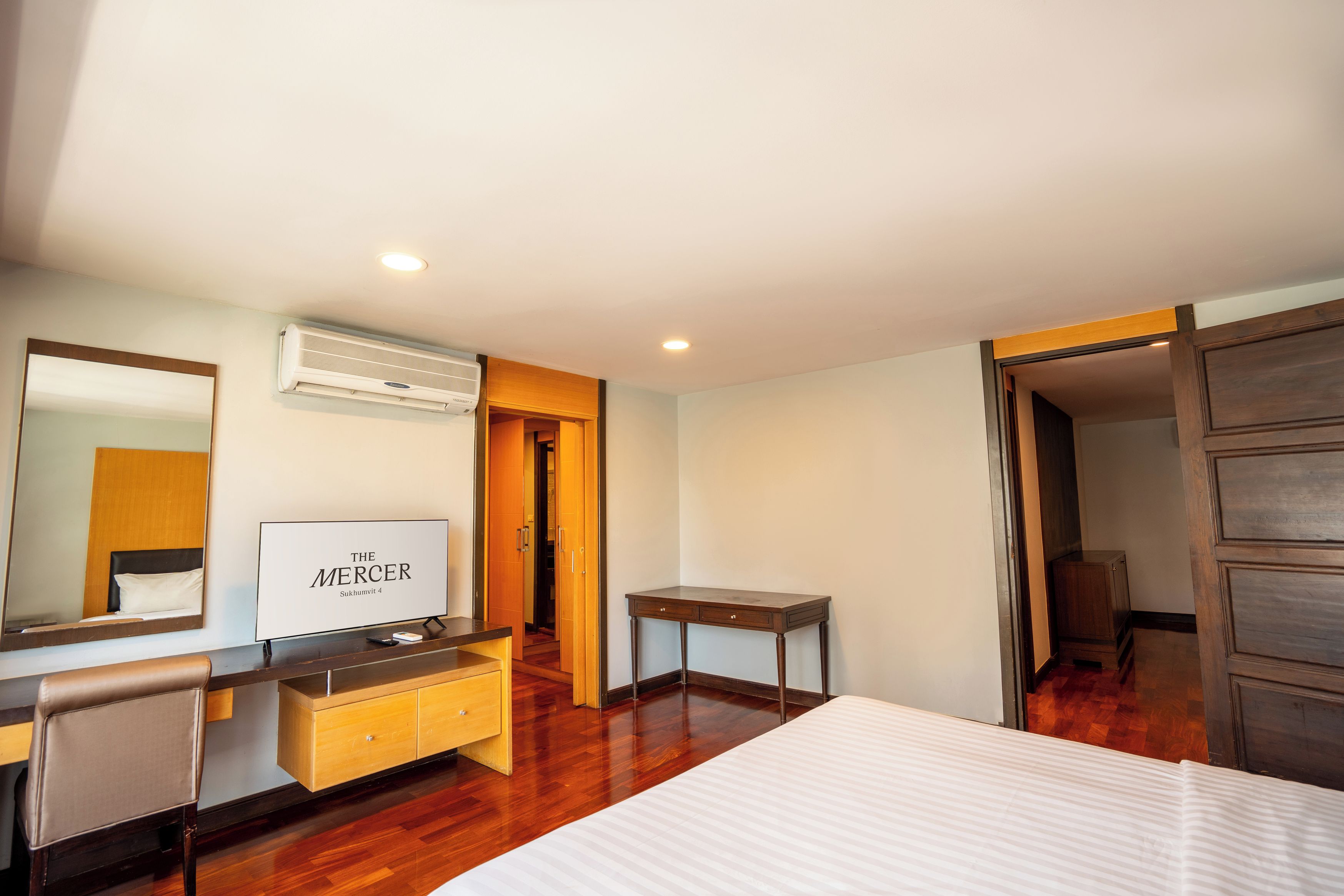 A hotel room with a bed, a desk, a chair, a TV, and an air conditioning unit.