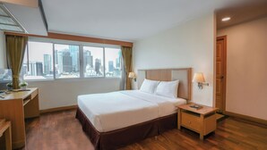 Habitación de hotel con una cama grande, un escritorio, una silla, una mesita de noche y vistas de la ciudad a través de la ventana.