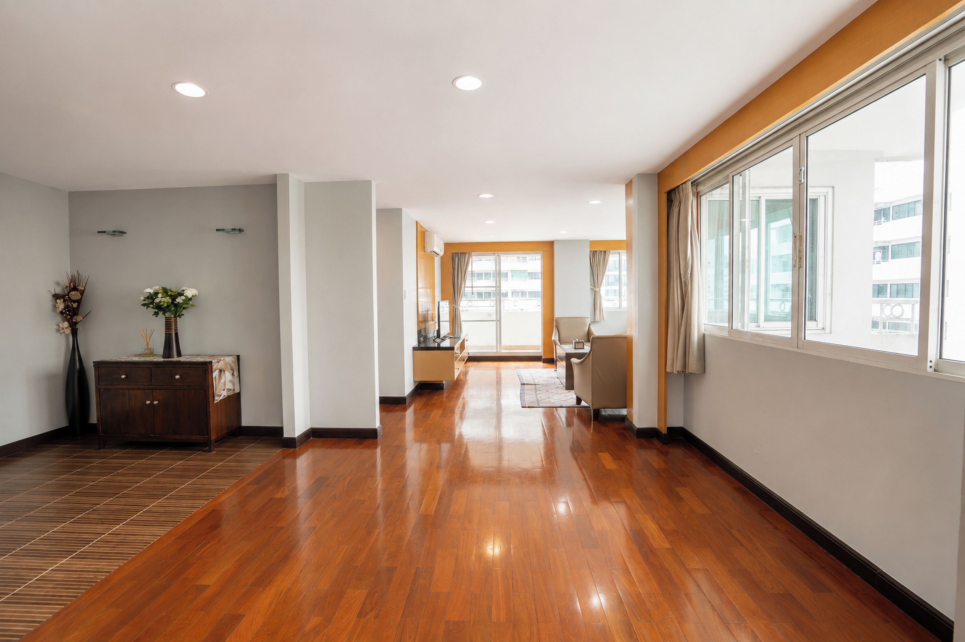 A hotel corridor with wooden flooring, a reception desk, and a large window offering a view of the building.