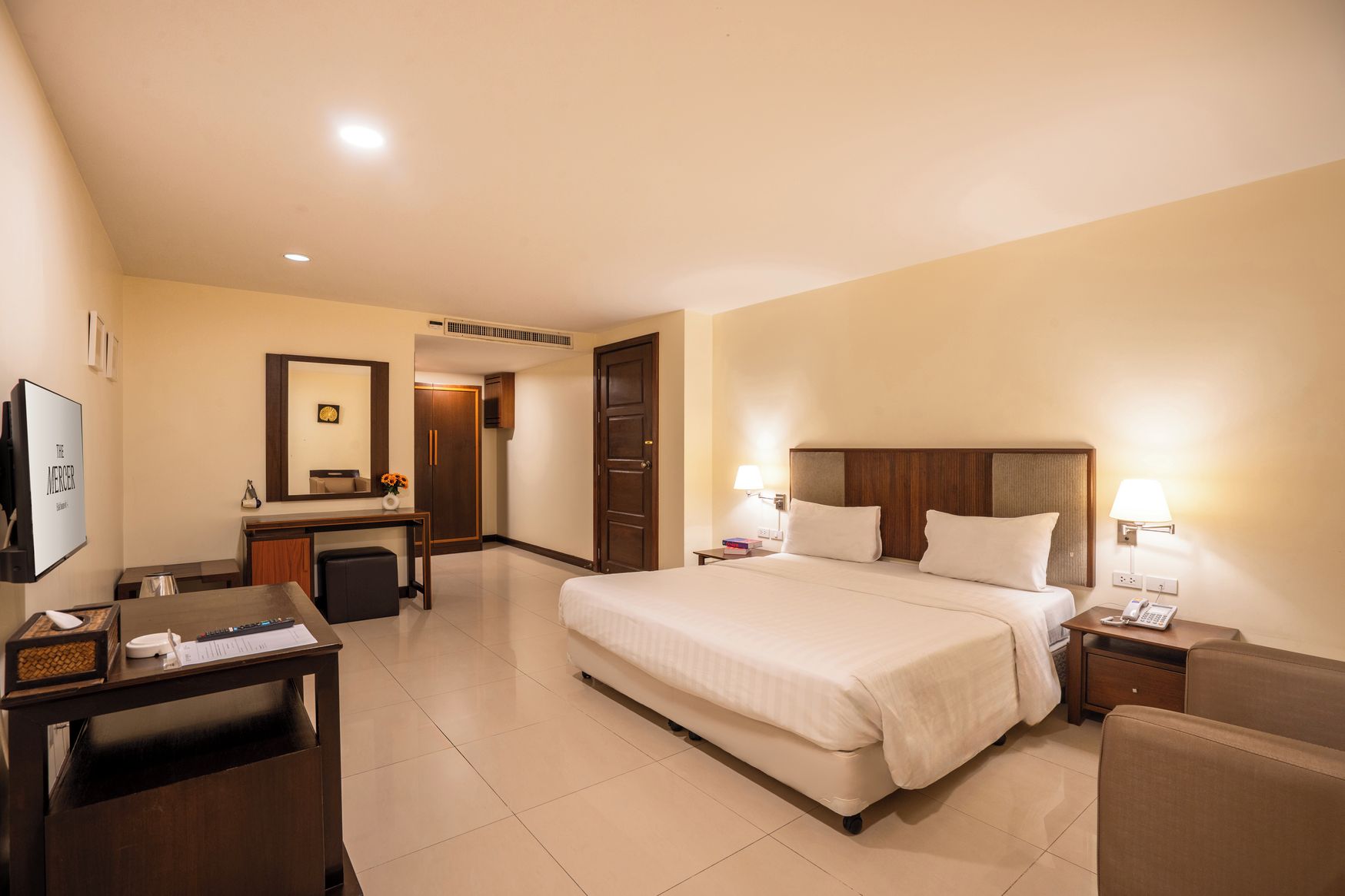 Una habitación de hotel con cama, mesitas de noche, un escritorio, un espejo y una puerta.