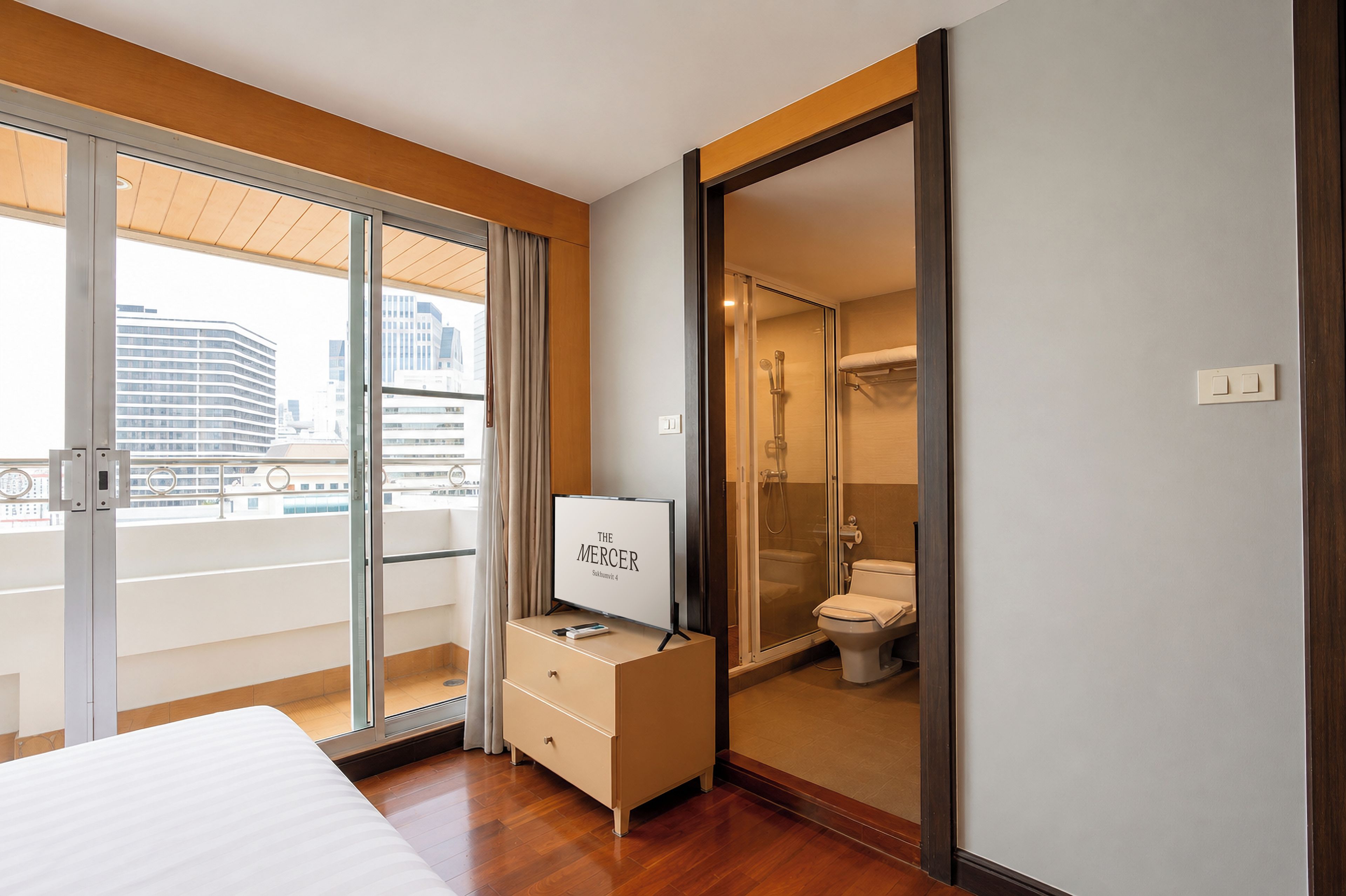 A hotel room with a bed, a TV on a dresser, a sliding glass door to the bathroom, and a city view.