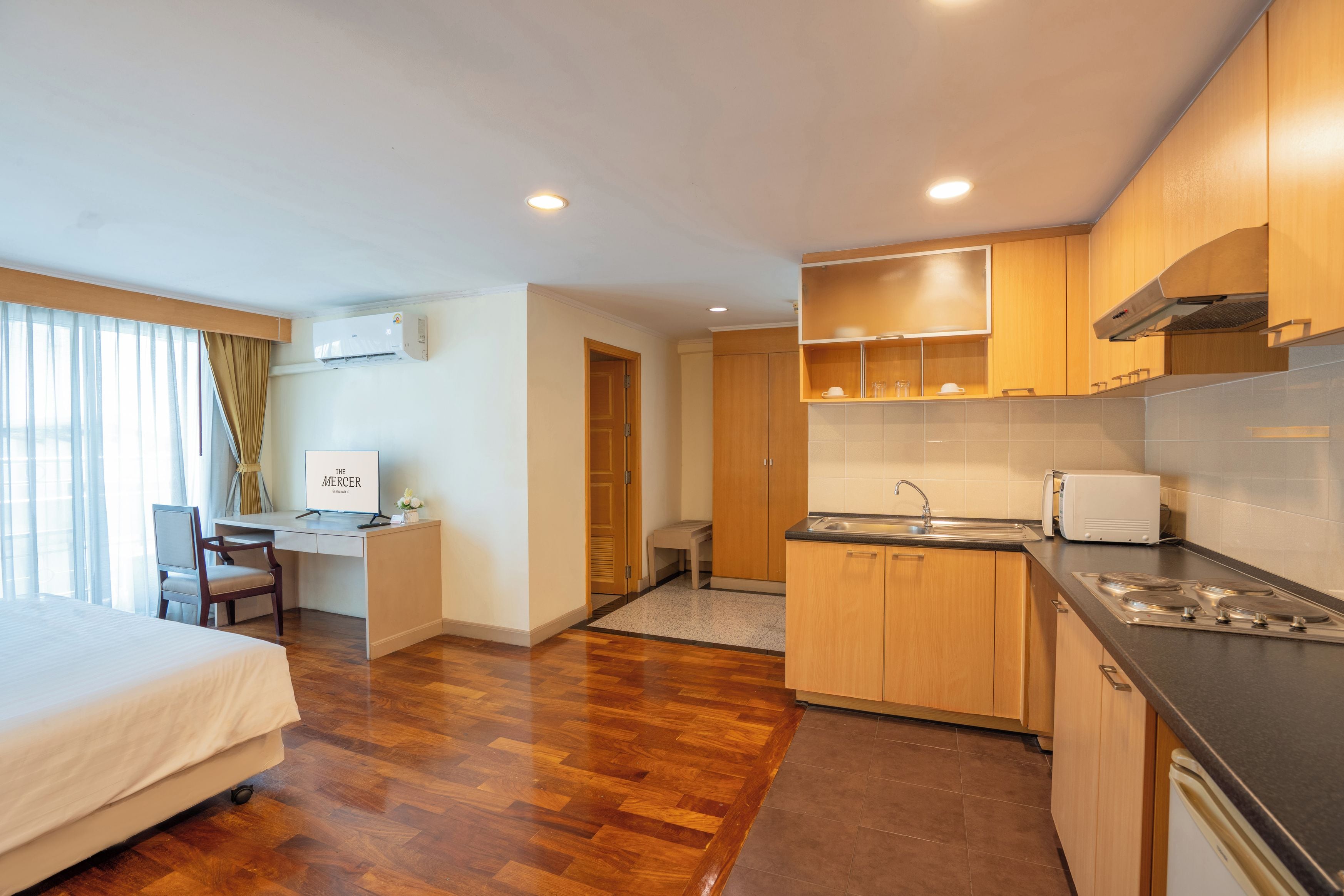 A hotel room with a bed, desk, chair, kitchenette, and a bathroom.