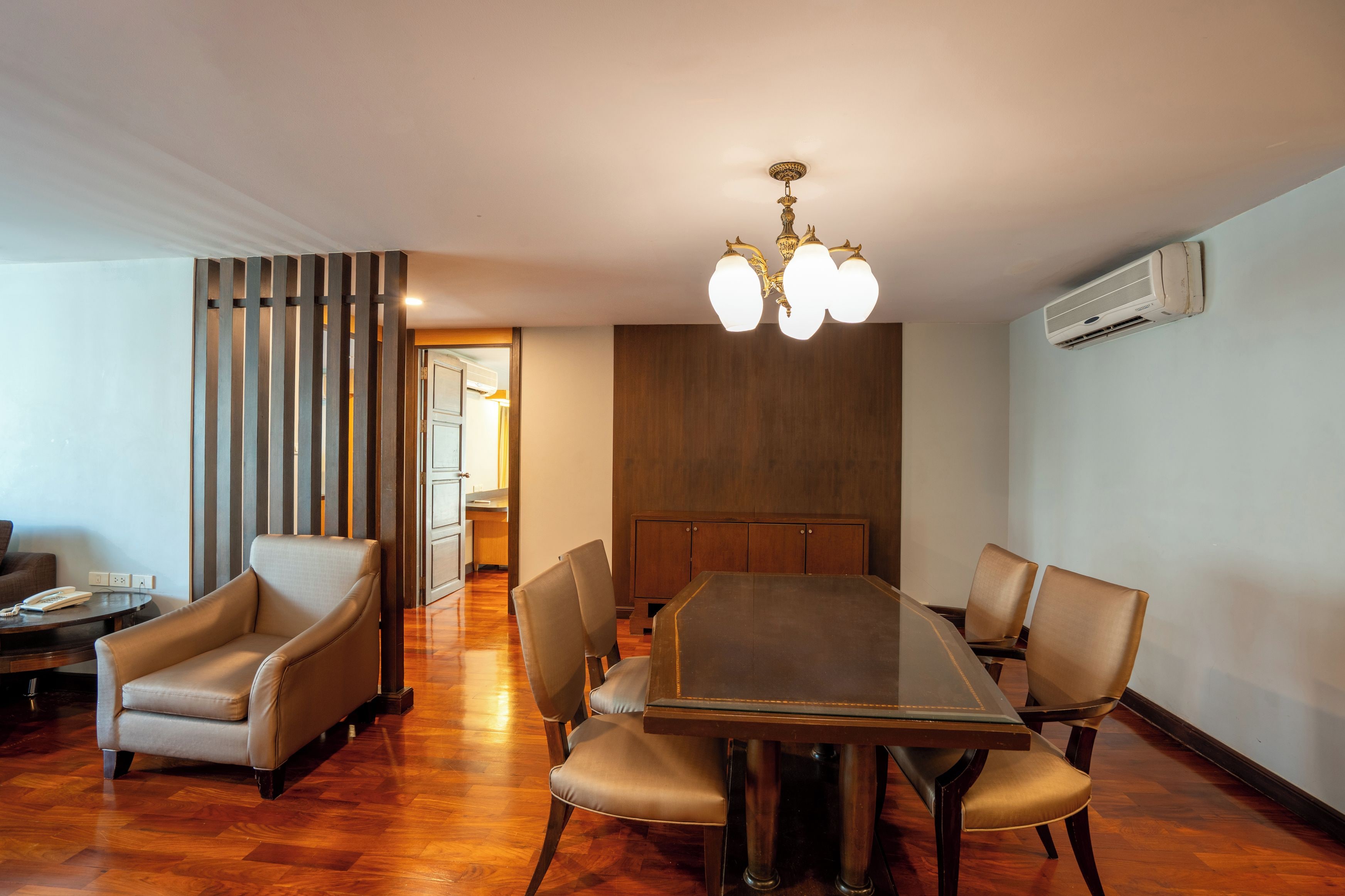 A dining area with a wooden table and six chairs, a chandelier, and an air conditioning unit on the wall.